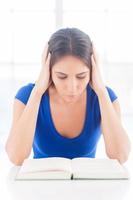Reading a boring book. Frustrated young woman reading a book and holding head in hands photo
