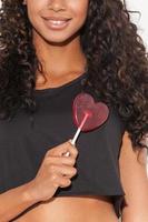 Candy heart. Cropped image of young African woman holding candy in front of her heart and smiling while standing against white background photo