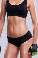 Fit curves. Close-up of young sporty woman with perfect body standing against grey background photo