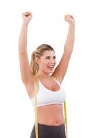 Worked off the excess weight. Happy young woman with measuring tape on her shoulders raising hands up and smiling while standing isolated on white photo