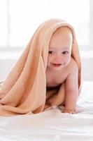 Fresh and happy baby. Happy little baby covered with towel smiling while sitting in bed photo