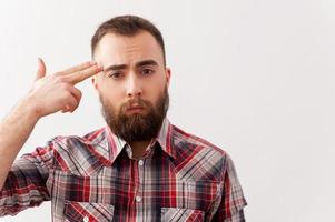 Depressed and frustrated. Depressed young man in casual wear touching his temple with finger gun photo