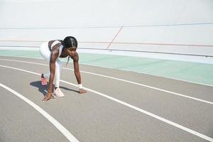 Beautiful young African woman standing at starting position on running track outdoors photo