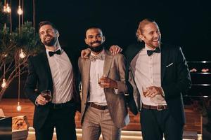 Three handsome men in suits bonding and drinking whiskey while spending time on party photo