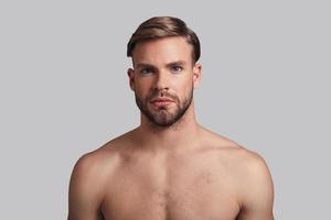 Just the way he is. Handsome young man looking at camera while standing against grey background photo