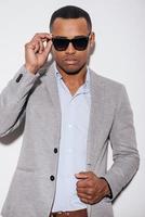 Trendy handsome. Confident young African man in sunglasses adjusting his jacket and looking at camera while standing against white background photo