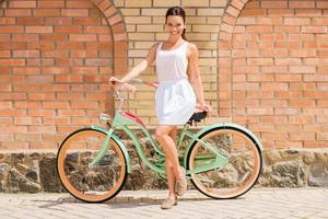 belleza con bicicleta vintage. toda la longitud de una atractiva joven sonriente parada cerca de su bicicleta vintage foto