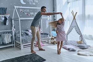 Spontaneous dance. Full length of father and daughter holding hands and smiling while dancing in bedroom photo