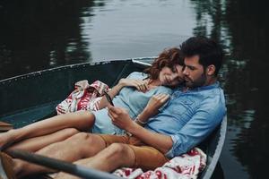 Two hearts full of love. Beautiful young couple listening music while sitting in the boat outdoors photo
