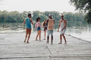 totalmente despreocupado. toda la longitud de los jóvenes en ropa casual sonriendo y divirtiéndose mientras están de pie en el muelle foto