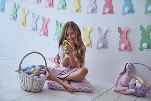 Feeling playful.  Cute little girl playing with duckling and smiling while sitting on the pillow with decoration in the background photo