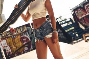 Skater girl. Close-up of beautiful young woman holding her skateboard while spending time outdoors photo