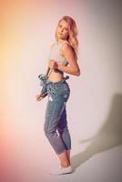 Casual style. Full length studio shot of beautiful young woman stretching her jeans overall and looking at camera photo