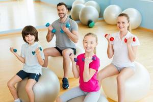 Enjoying time in sorts club. Top view of happy sporty family exercising with dumbbells in sports club while sitting on the fitness balls together photo