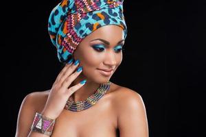 belleza africana. hermosa mujer africana con un pañuelo en la cabeza y un collar y mirando hacia otro lado mientras está de pie contra el fondo negro