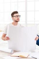 Thinking about new project. Thoughtful young man examining blueprint while sitting on the floor at home photo