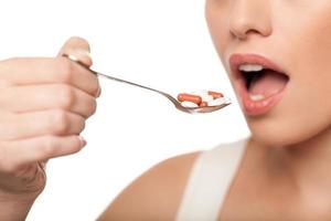 Woman taking pills. Cropped image of young woman holding a spoon full of pills and keeping mouth open while isolated on white photo