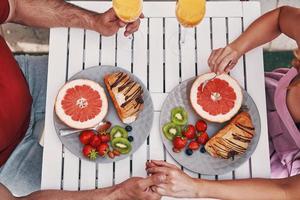 cerrar la vista superior de una pareja joven amorosa con ropa informal tomándose de la mano mientras desayuna foto