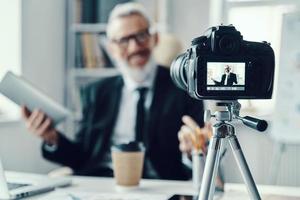 Confident mature man in elegant suit telling something and gesturing while making social media video photo