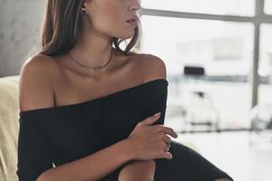 Elegant in everything. Close up of young woman in elegant black dress resting while sitting on the sofa photo