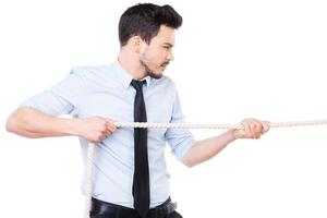 Strong and confident business leader. Side view of confident young man in shirt and tie pulling a rope while standing against white background photo