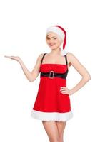 Your advertisement in her hand. Beautiful young woman in Santa costume holding a copy space and smiling while standing isolated on white photo