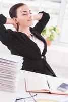 tiempo de enfriamiento. vista lateral de una alegre joven mujer de negocios sosteniendo la cabeza en las manos y manteniendo los ojos cerrados mientras se sienta en su lugar de trabajo foto