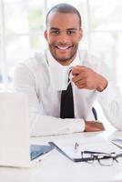 Coffee break. Handsome young man in shirt and tie drinking coffee and smiling while sitting at his working place photo