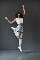 Beauty in the mid-air. Full length of attractive young woman looking at camera and smiling while jumping against grey background photo