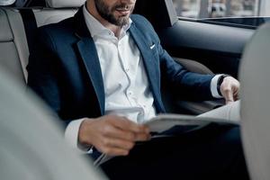 Latest business news. Close up of young man in full suit reading a newspaper while sitting in the car photo