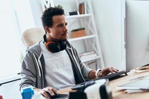 Computer hacker. Concentrated young man in casual clothing using computer while spending time at home photo