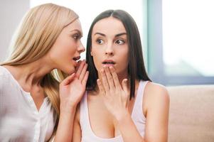 contando los últimos chismes. dos hermosas mujeres jóvenes chismeando mientras una de ellas cubre la boca con la mano foto