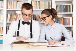 Studying together. Cheerful young nerd couple in glasses preparing to exams while sitting together at the library photo