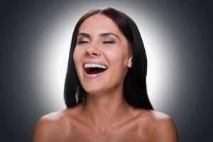 Pure happiness. Portrait of beautiful young shirtless woman keeping eyes closed and smiling while standing against grey background photo