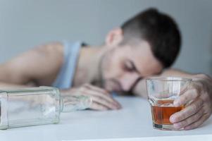 olvidando sus problemas. joven sentado en la mesa con una botella vacía y manteniendo los ojos cerrados foto