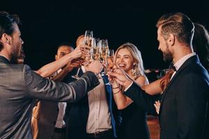 grupo de personas hermosas en ropa formal brindando con champán y sonriendo mientras pasan tiempo en una fiesta de lujo foto