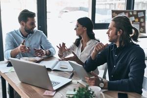 Discussing risky ideas. Group of young modern people in smart casual wear working together and smiling while sitting in the creative office photo