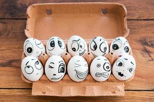 Together we are stronger. Top view of funny eggs with different emotions laying in container on the wooden desk photo