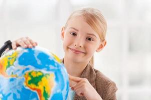 elegir un punto de viaje. niñita alegre con ropa formal examinando el globo con una lupa mientras se sienta en la mesa foto