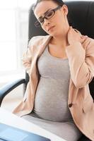 Tired pregnant woman. Depressed pregnant businesswoman holding head in hand while sitting at her working place in office photo