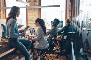 Group of young modern people in smart casual wear communicating and using modern technologies while working in the office photo