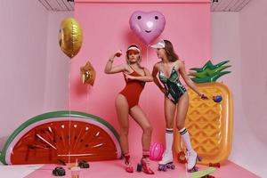 On the way to perfect shape. Full length of two playful young women in swimwear exercising while standing against pink background photo