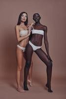 Extremely beautiful. Full length of two attractive mixed race women looking at camera while standing against brown background photo