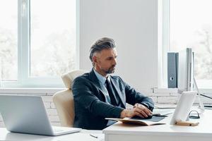 Confident mature man in formal business wear using computer while sitting at his working place photo