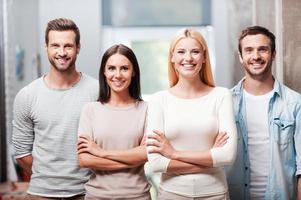 Young and successful team. Four young business people in smart casual wear standing close to each other and smiling discussing photo