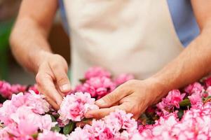 Gardener. Cropped image of man in apron taking care of flowers while standing in greenhouse photo