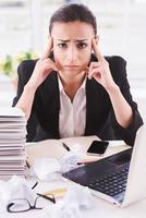 Tired businesswoman. Young business woman holding head in hands and looking at camera while sitting at her working place photo