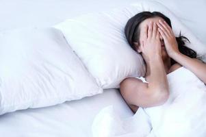 Depressed women in bed. Top view of young sad women lying on the bed and hiding her face in hands photo