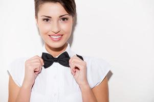 Confident and stylish. Beautiful young short hair woman in white shirt and suspenders adjusting her bow tie and looking at camera photo