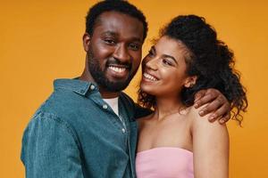 hermosa joven pareja africana abrazándose y sonriendo mientras se enfrenta a un fondo amarillo foto